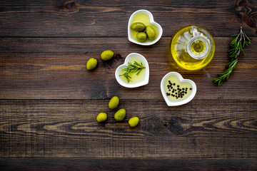 Oil on the kitchen table. Extra virgin olive oil in glass jar near green olives and branch of rosemary on dark wooden background top view copy space