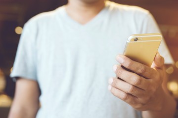 Close up of a people man hand holding using mobile smart phone stand cellphone  in cafe coffee shop. with filter Tones vintage effect ,Warm tones.