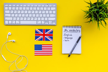 Learn new english vocabulary. Learn landuage concept. Computer keyboard, british and american flags, notebook for writing new vocabulary on yellow background top view