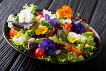 Portion of salad with edible flowers with fresh lettuce, spinach, tomatoes and cheese close-up. horizontal