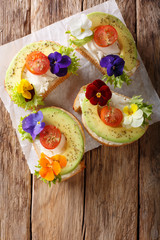 Festive toasts with avocado, tomatoes, edible flowers and cream cheese close-up. Vertical top view