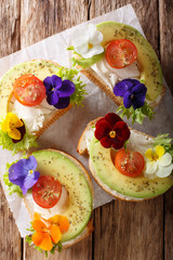 Healthy food: toasts with avocado, tomatoes, edible flowers and cream cheese close-up. Vertical top view