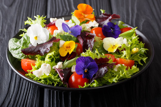Beautiful healthy salad with edible flowers with fresh lettuce, spinach, tomatoes and cheese close-up. horizontal