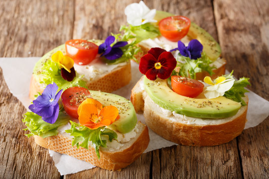 Sandwiches with edible flowers, fresh avocado and cream cheese close-up. horizontal