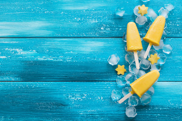 Yellow mango ice cream on a stick on a blue wooden background.