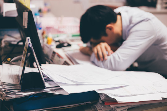 Stressful and frustrated young Asian business office worker having overwork problem crisis with tons of paperwork load.