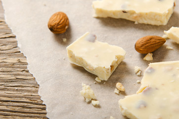 White chocolate scattered on white parchment paper with nuts. Sweet dessert