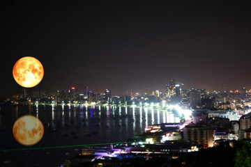 super full blood moon reflection on sea colorful of blur night light over city
