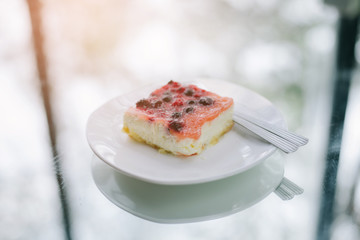 Slice of cheesecake topped with cherry compote on plate on brown table with dessert fork, top view