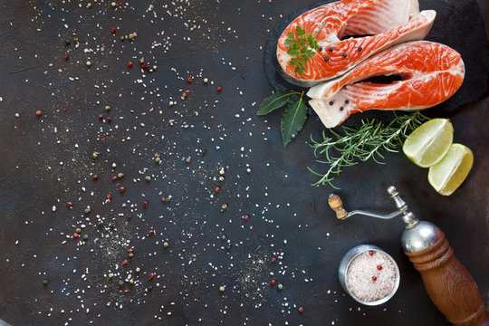 Close-up photo of fresh salmon fish with sea salt and lime slices on black table background