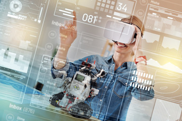 Progressive woman. Creative electric engineer smiling while wearing virtual reality device and working on her robot