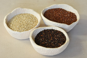Organic red quinoa, organic white quinoa and organic black quinoa in rustic hand made clay bowls on a canvas covered surface