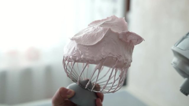 Hands of a female confectioner hold a steel whisk from a mixer, covered with a pink sweet mass of strawberry marshmallow. Delicious dessert.Homemade sweet.Homemade marshmallow dessert.Pink zefir