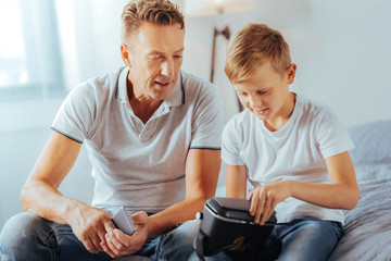 Modern developments. Cheerful nice smart boy sitting together with his father and holding 3d...