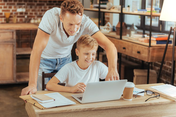 Modern device. Cheerful happy smart by sitting at the laptop and looking at its screen while being at home