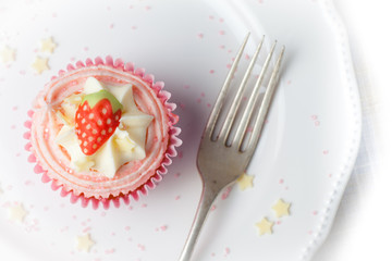 Pink strawberry cupcake on white plate with star sprinkles , overhead