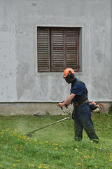 Lawn mower worker cutting grass in green field with trimmer