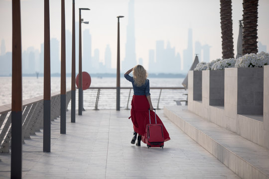 Beautiful woman in a red dress comes with a suitcase.