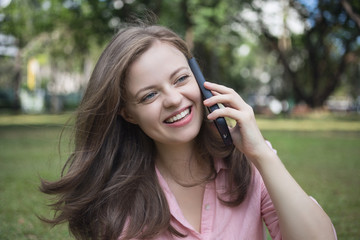 Young caucasian woman talking on the phone, looks happy. Outdoor picture