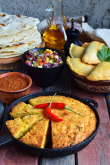 Cornbread and other mexican food - tacos, salsa with tomato, red onion, lime, cilantro, corn and hot pepper sauce, empanadas. Copy space.