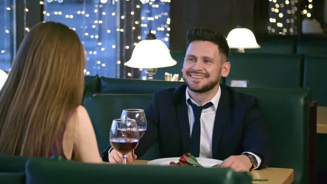 Medium shot with slowmo of cheerful man in suit laughing and talking with unrecognizable woman on dinner date in restaurant