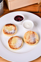 Traditional russian breakfast fried cottage cheese with cherry jam, sour cream and black tea. Top view cheese pancake, close.