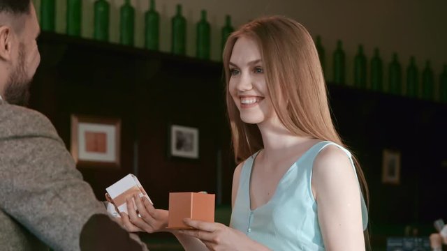 Slowmo of ecstatic young woman opening present from her boyfriend and laughing while on romantic date in cafe