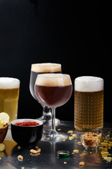 Ale, stout and lager beer in glasses with snacks and sauce on sunlit metallc table