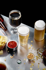 Ale, stout and lager beer in glasses with snacks and sauce on sunlit metallc table