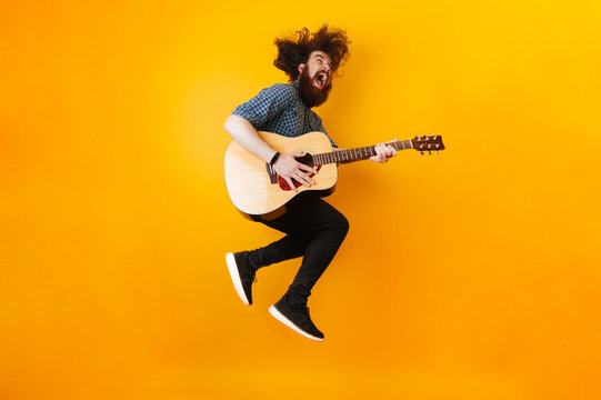 Crazy Bearded Man With Guitar Jumping Over Yellow Background