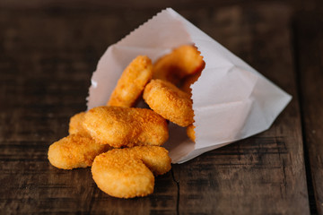 Fried chicken nuggets in a paper bag on wood background