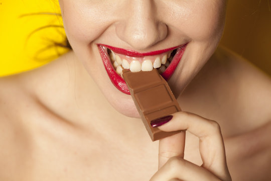 Young beautiful woman eating a chocolate on yellow background