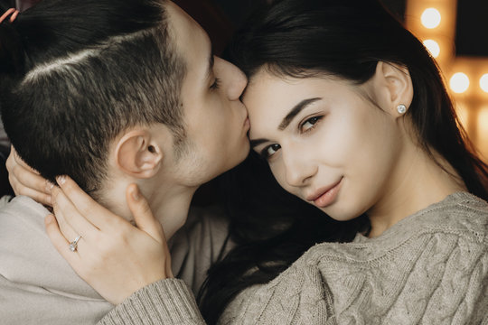 Close up portrait of lovely couple while boy is kissing her girlfriend on forehead and she is looking into camera.