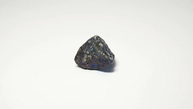 Macro shot of bornite mineral isolated over white background and spinning around
