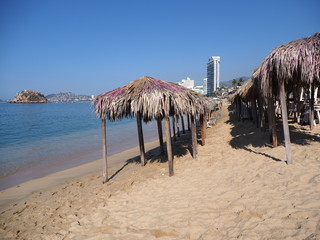 Exotic bamboo huts on sandy beach at bay of ACAPULCO city in Mexico with skycraper and waves of...