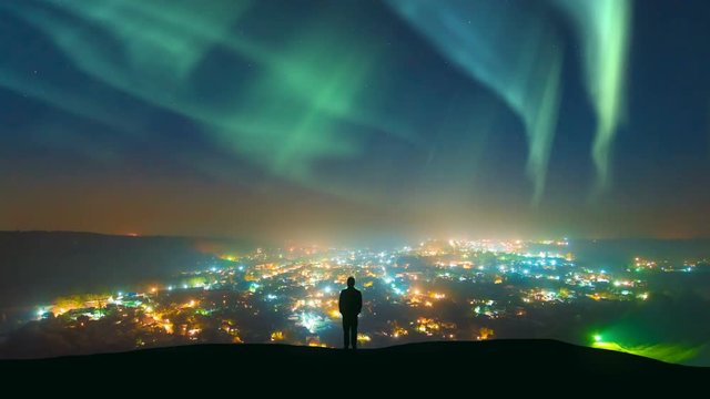 The man standing against the northern light over the night city. time lapse