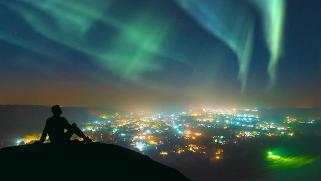 The man sitting against the northern light over the night city. time lapse