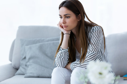 Thoughtful young woman sitting on sofa at home.