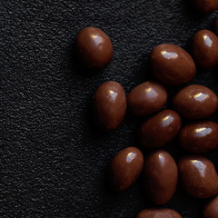 Chocolate candy background. Dark brown chocolate round candies on black concrete background  top view, close up.