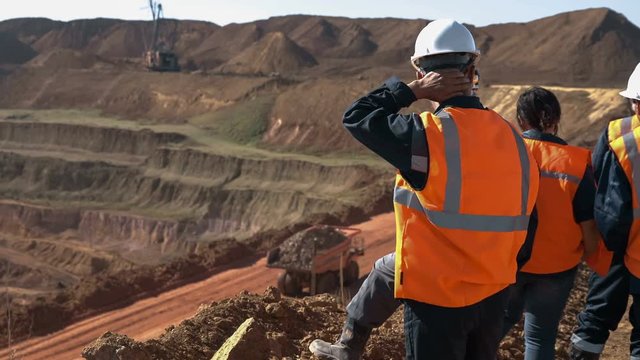 Panorama shot of a group of workers in overalls actively speaking on board a bauxite quarry.