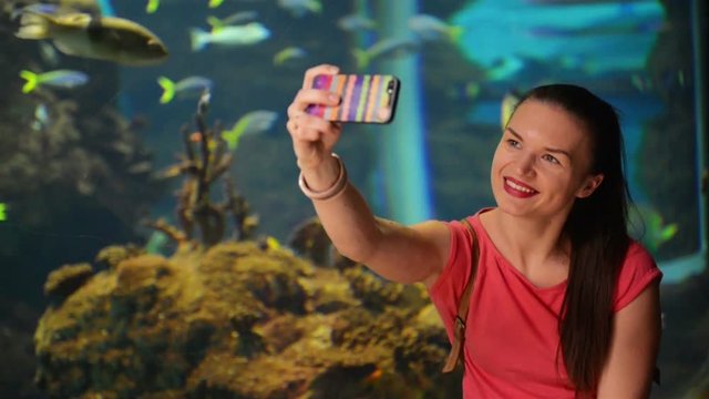 Young Girl is Taking Selfie. Aquarium with Fishes Is on Background. She is Very Happy and Cheerful and Having a Lot of Fun.