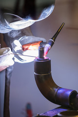 Naklejka premium Working welder in a mask with glass connects the metal by welding in the factory