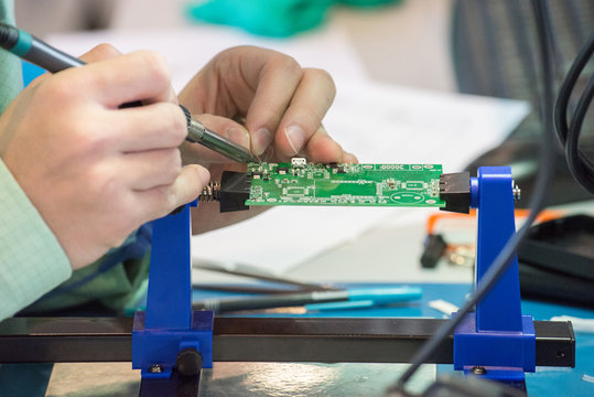 A person solder the parts of the chip with a soldering iron with tin