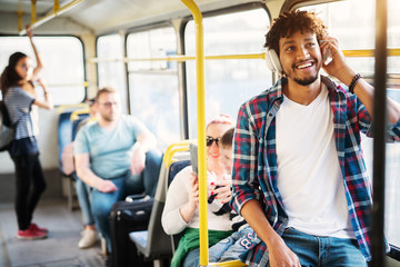 A group of people traveling by the bus with a young cheerful handsome man in the first plan of the picture who is listening to music on his headphones and smiling.