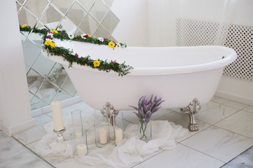 The luxurious bathroom is decorated with flowers and candles. With a big mirror.