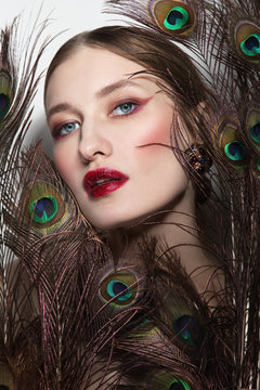 Glamorous portrait of young beautiful woman in peacock feathers