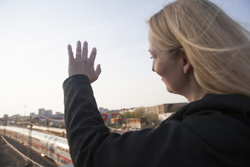 Mujer de negocios saludando con la mano. Abajo un tren se va (fuera defoco)