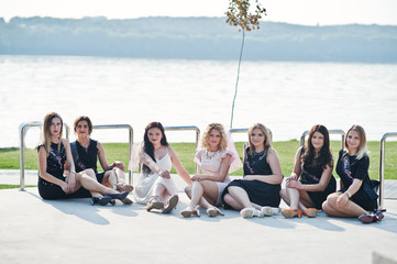Group of 7 girls wear on black and 2 brides sitting background lake at hen party.