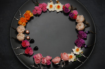 Mix of Fake Colorful Plastic Mini Flowers Earings Black Round Plate Copy space. Craft, Art, Hobby concept.