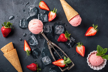 Flat lay with strawberry ice cream, berries and waffle cones on black background. Top view.